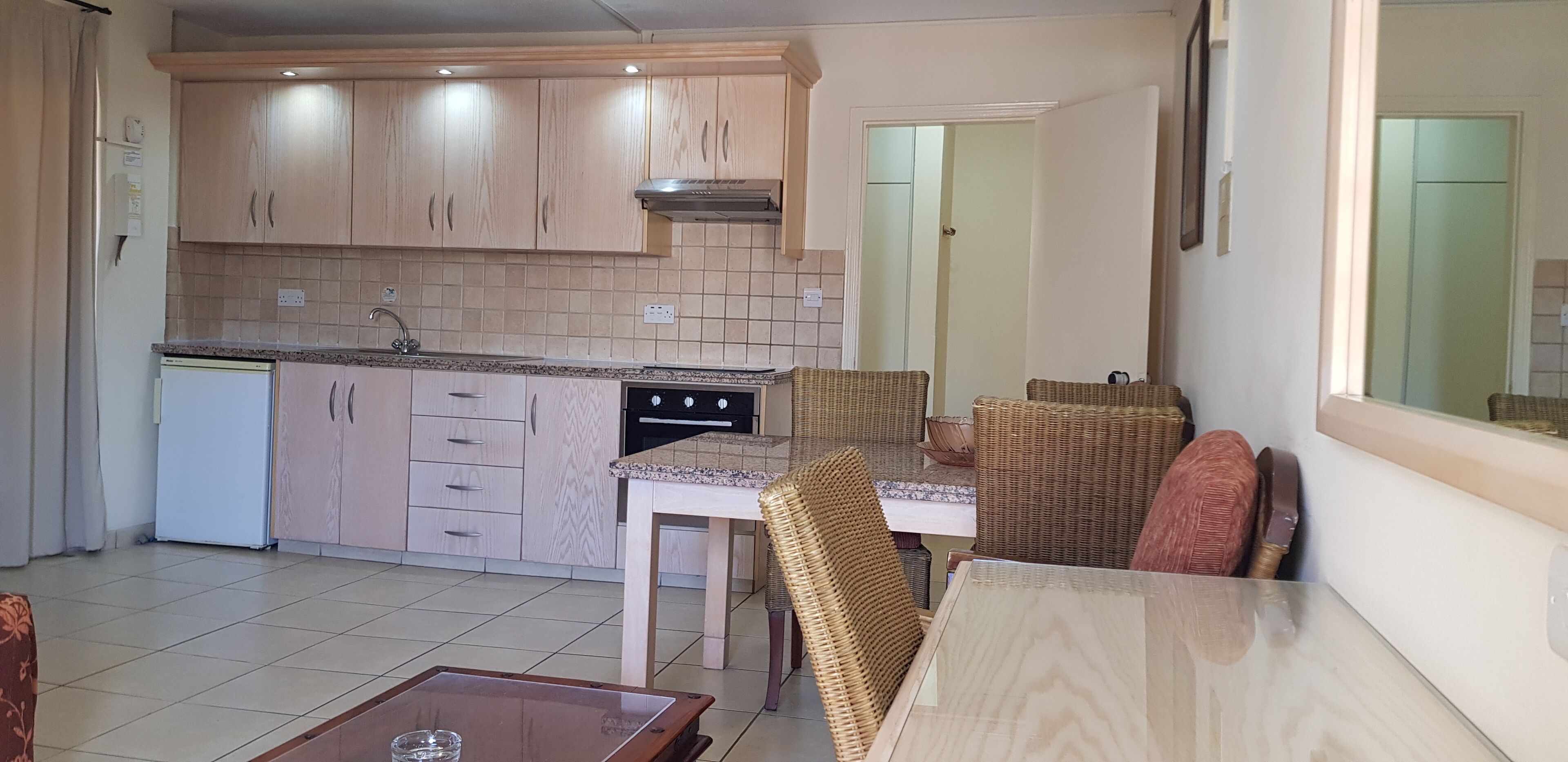 A compact kitchen with wooden cabinets, a built-in oven, and a dining area with wicker furniture.