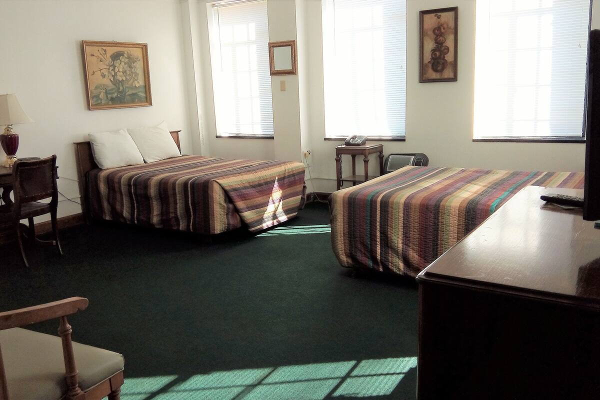 Une chambre d’hôtel avec deux lits, un bureau, une chaise et un téléviseur.