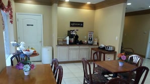 A dining area with wooden tables and chairs, a coffee station, and a kitchen in the background. - La Copa Inn (Alamo)