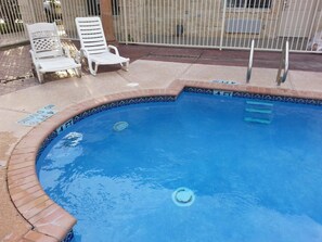 A swimming pool with a tiled edge, two white lounge chairs, and a metal fence in the background. - La Copa Inn (Alamo)