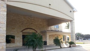 A two-story building with a stone facade, a covered entrance, and a landscaped area with palm trees. - La Copa Inn (Alamo)