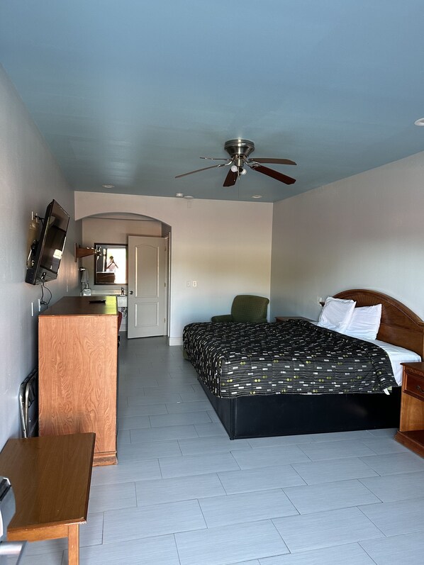 Habitación de hotel con cama, escritorio, silla, ventilador de techo y televisor montado en la pared.