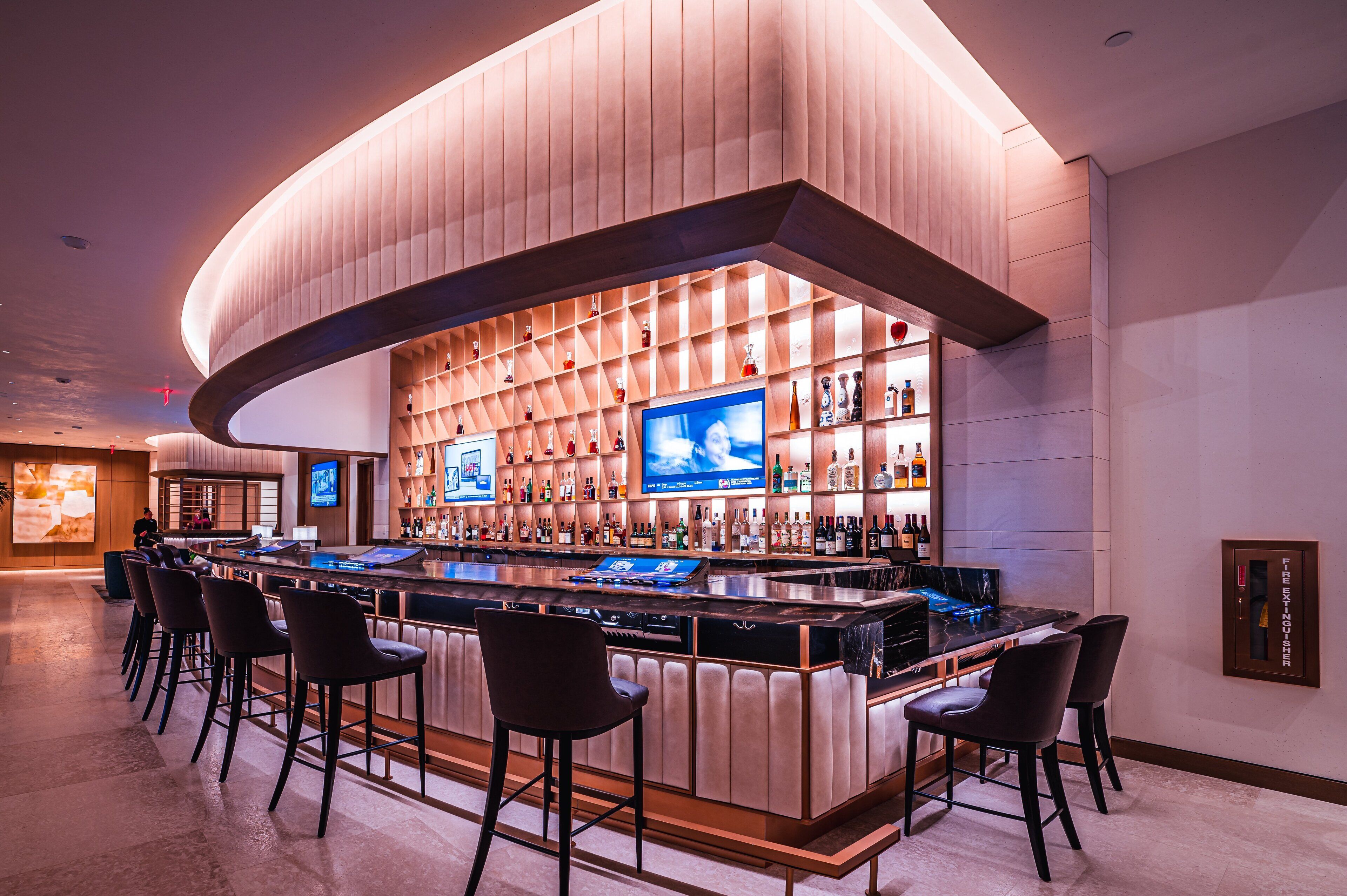 A modern bar area with a curved counter, multiple bar stools, and a wall of liquor bottles.