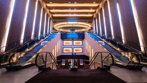 Un hall d’hôtel moderne doté d’un atrium central, de plusieurs niveaux d’escalators et d’un espace de réception bien visible.