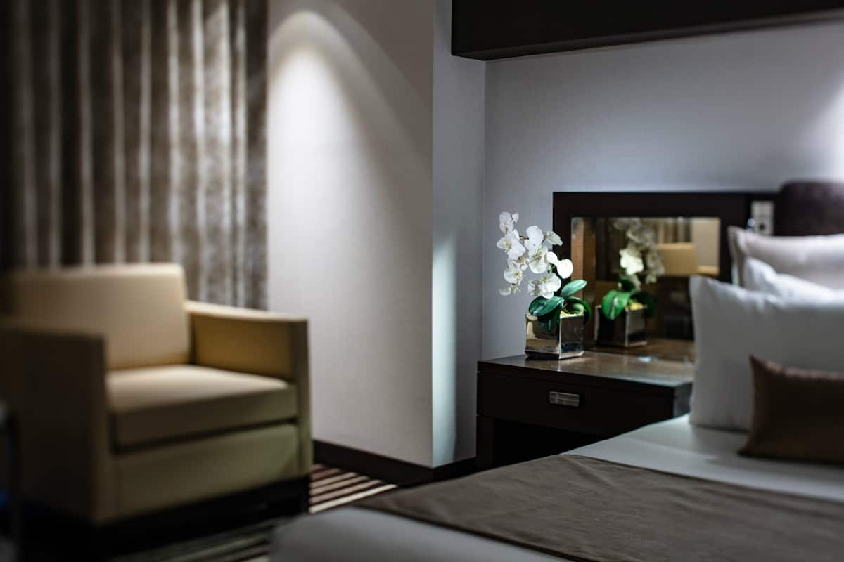 Een moderne hotelkamer met een bed, nachtkastje, lamp, stoel en spiegel.