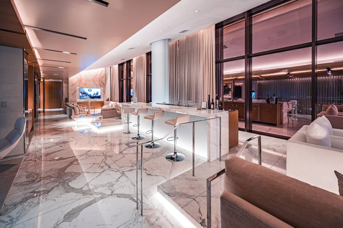 Een moderne hotellobby met een marmeren vloer, een bar met krukken en een groot televisiescherm.