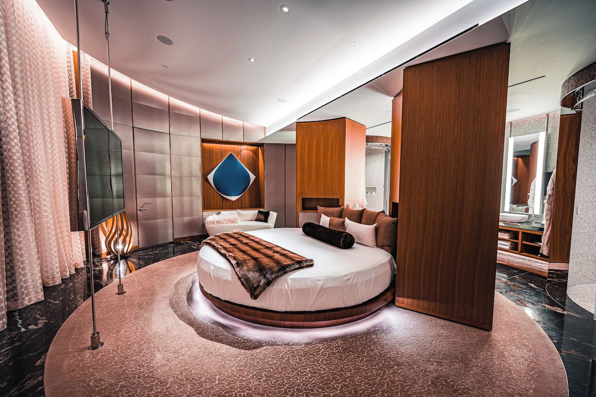 Een moderne slaapkamer met een groot bed, een spiegel en een houten garderobe.