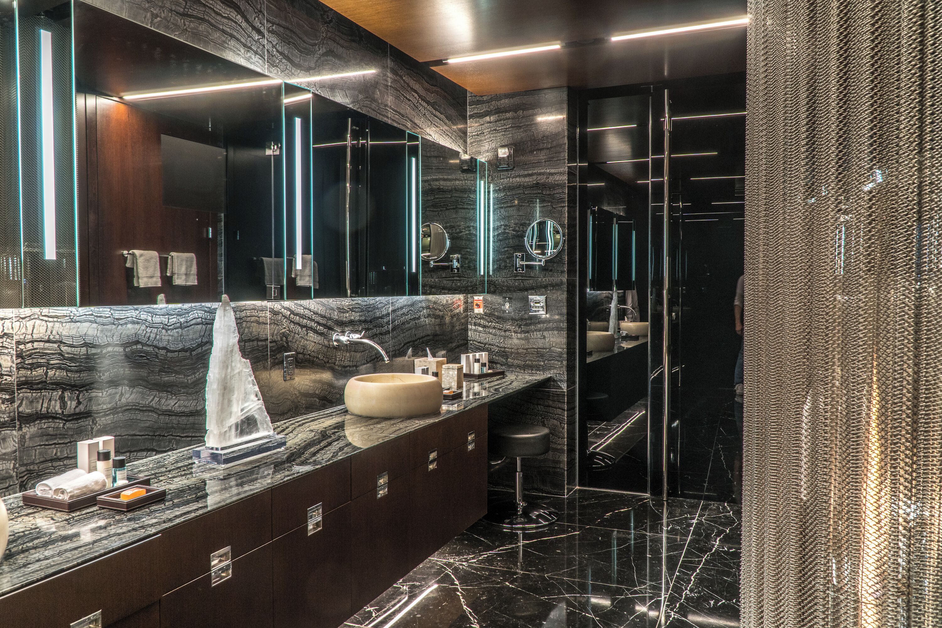 Un baño moderno con tocador de mármol, espejos amplios y cabina de ducha con mampara de vidrio.