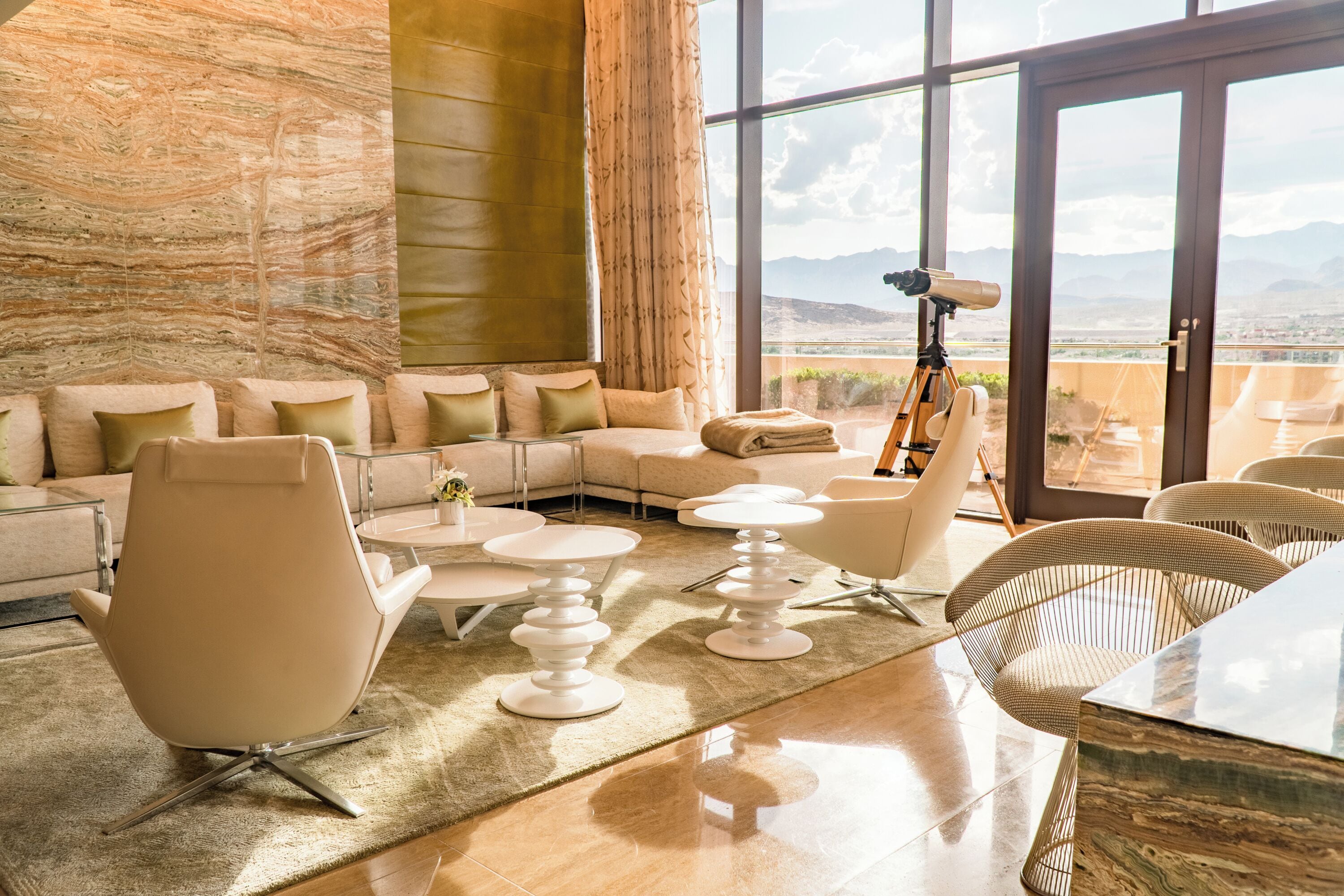 A modern living room with a large sofa, a coffee table, and a telescope on a balcony overlooking a mountainous landscape.