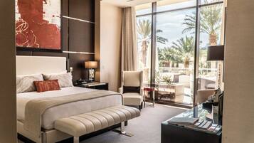 A modern hotel room with a large bed, a desk, and a view of palm trees through large windows.