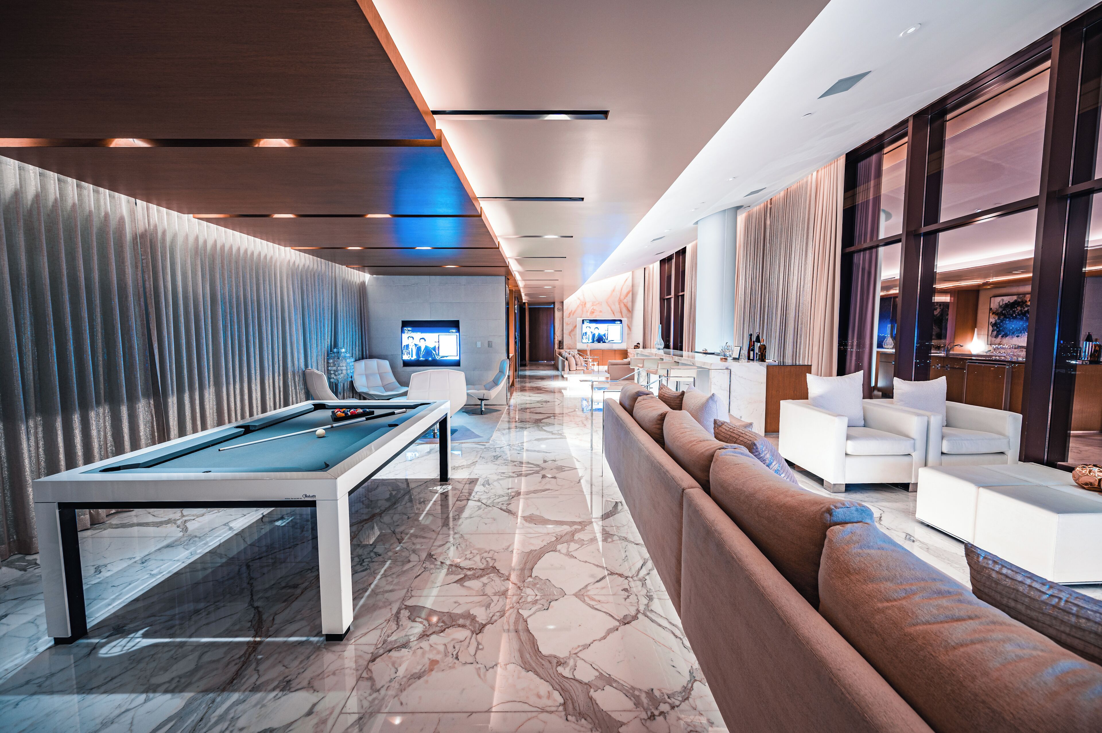 A modern lobby with a pool table, comfortable seating, and a TV screen.