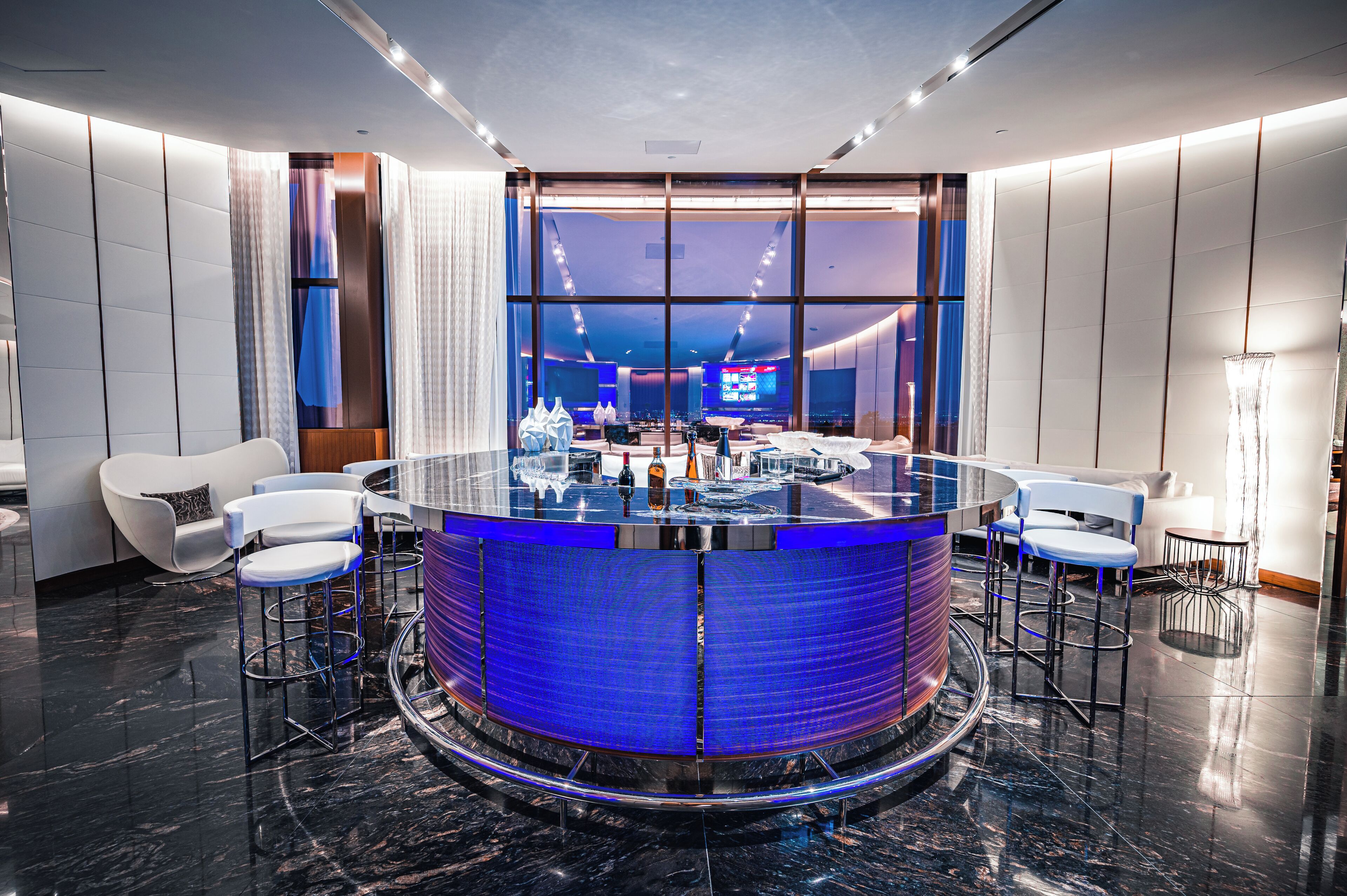 Un moderno espacio de bar con barra circular, asientos y un ventanal con vistas a la ciudad.