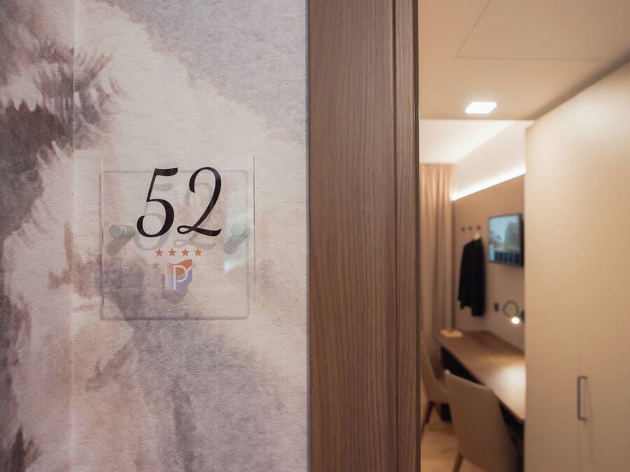 A hotel room with a number 52 sign on the wall, a wooden door, and a glimpse of a modern bathroom with a mirror and sink.