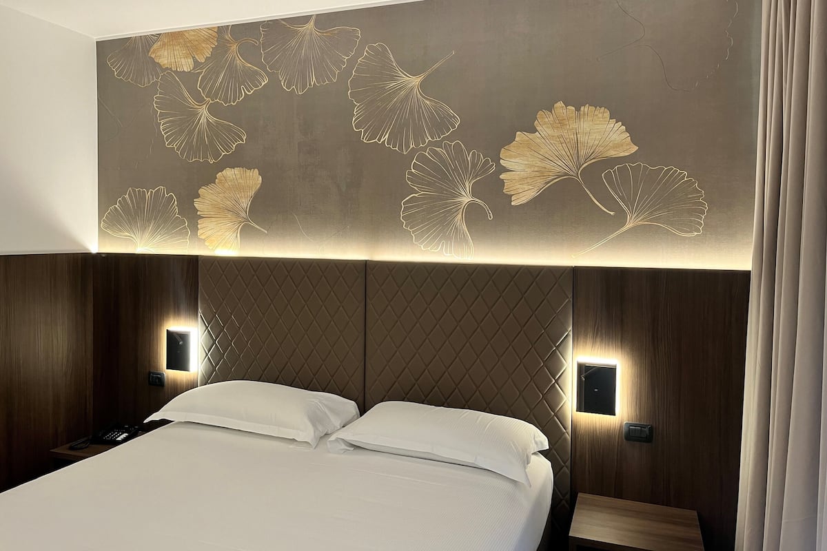 Una habitación de hotel con una cama, una pared con un diseño de hojas y dos lámparas de noche.