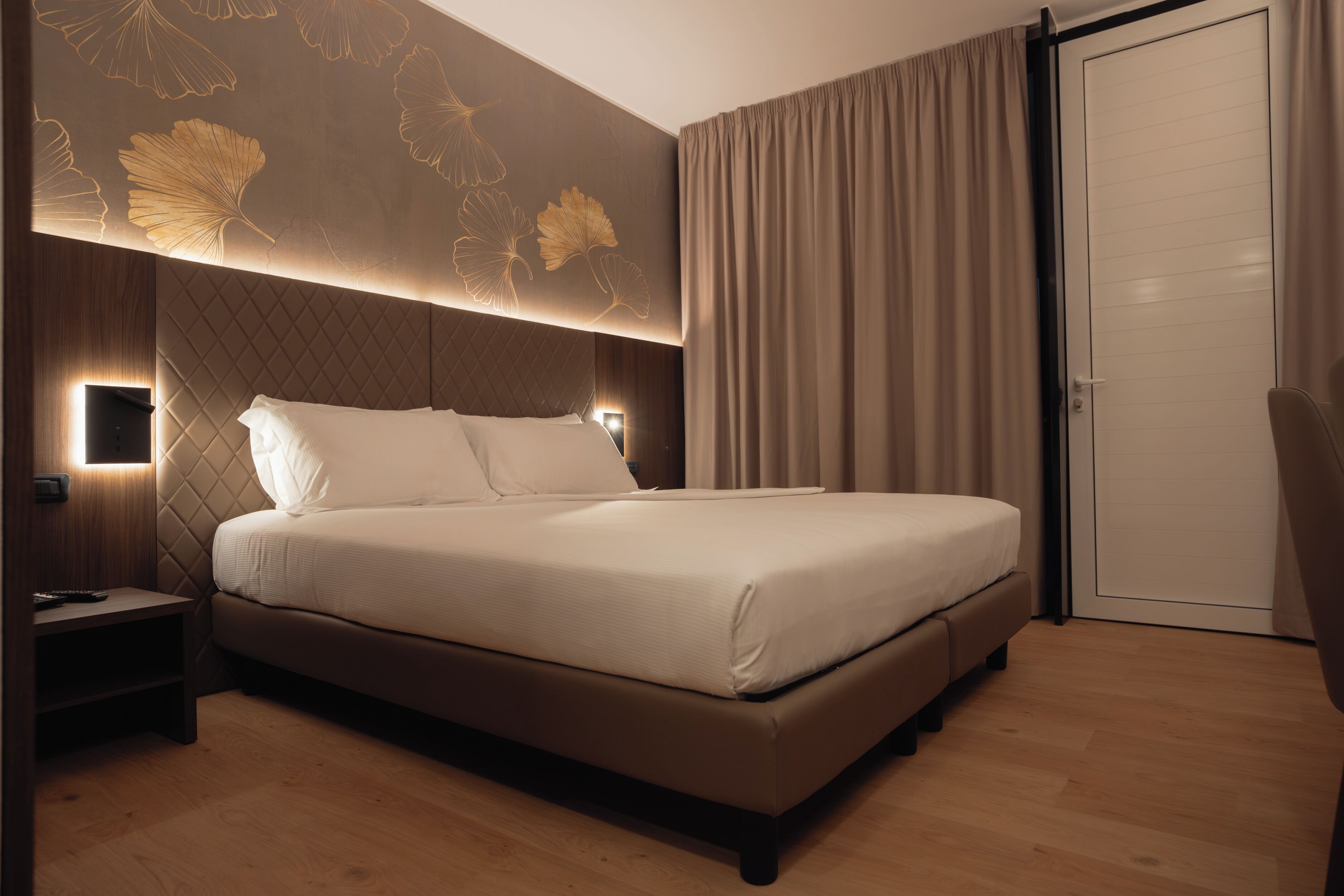 Una habitación de hotel moderna con una cama grande, una mesita de noche y un aplique en la pared.