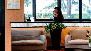 A reception area with a receptionist, two sofas, a potted plant, and a window with a view of trees.
