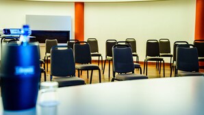 A conference room with rows of chairs, a projector screen, and a table in the foreground.