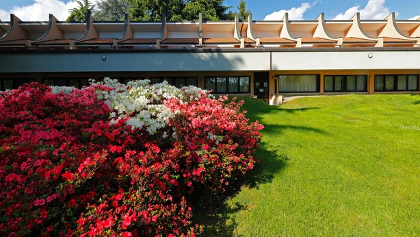A modern building with a flat roof and a large garden area with red and white flowers.