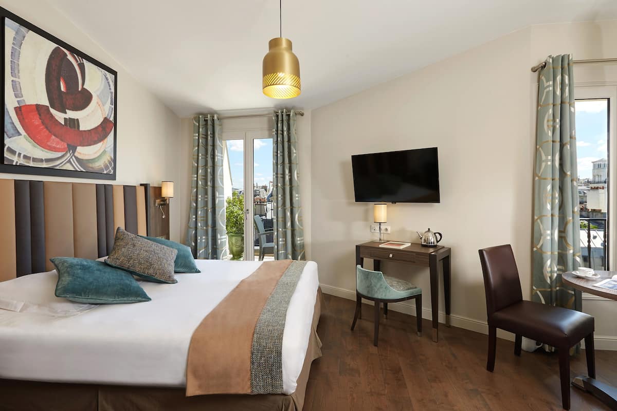 A hotel room with a large bed, a desk with a chair, a television, and a view of the city.
