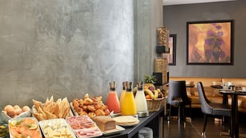 Un bufé de desayuno con diversas opciones de comida y bebidas, una zona de estar con sofá y sillones, y una pared moderna decorada con arte abstracto.