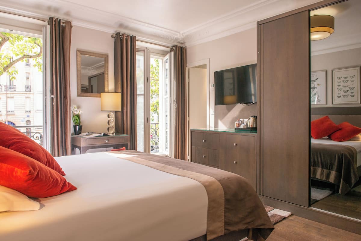 A hotel room with a large bed, a desk with a lamp, a wardrobe, and a television.