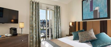A hotel room with a bed, a TV, a desk with a lamp, a coffee maker, and a view of the outdoors.