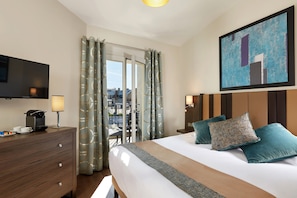 Habitación de hotel con cama, televisión, escritorio con lámpara, cafetera y vistas al exterior.