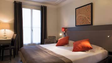 Habitación de hotel con una cama grande, dos almohadas, un escritorio con lámpara, una silla y una ventana con cortinas.