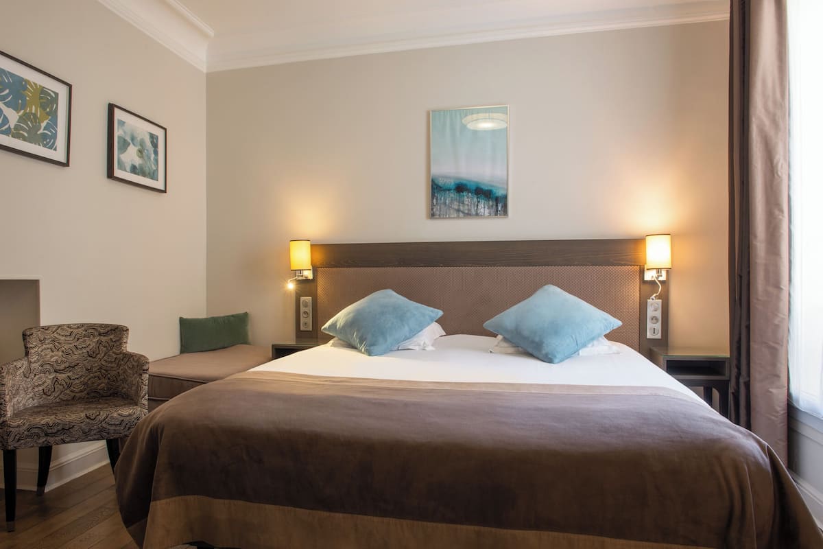 A hotel room with a large bed, two bedside lamps, a chair, and artwork on the walls.