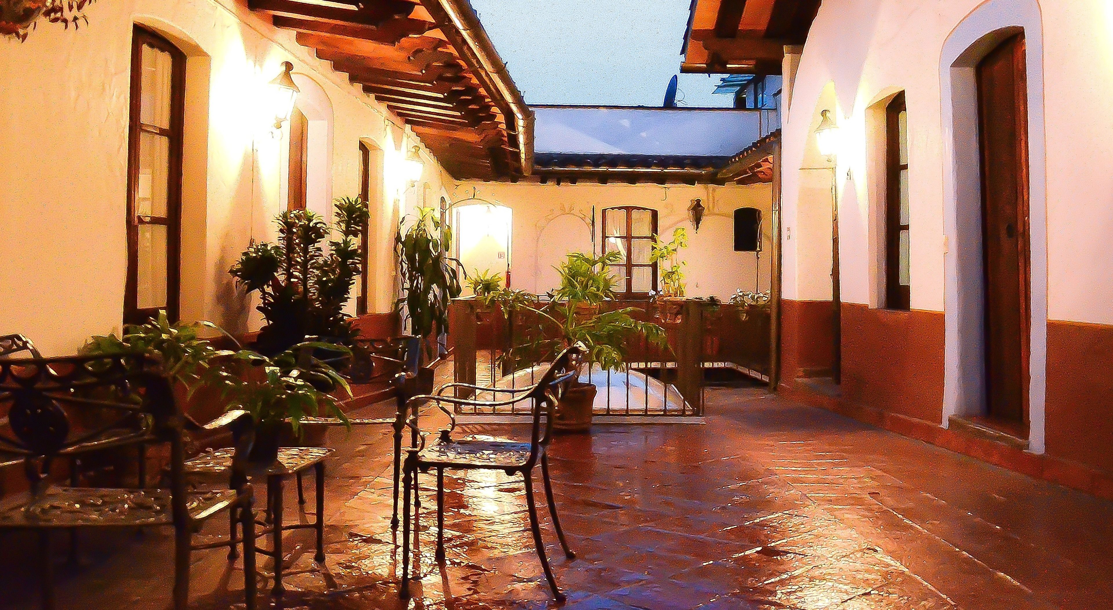 Un patio al aire libre con mesas y sillas, plantas en macetas y piso de baldosas.