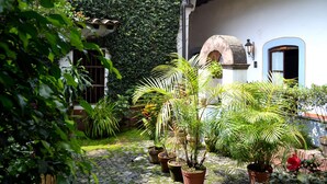 Une cour agrémentée de plantes en pot, un chemin pavé et un bâtiment doté d’un toit en tuiles et d’une arche en pierre.
