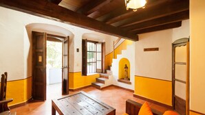 Une pièce avec une table en bois, des coussins orange, un escalier et une statue.