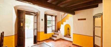 A room with a wooden table, orange cushions, a staircase, and a statue.