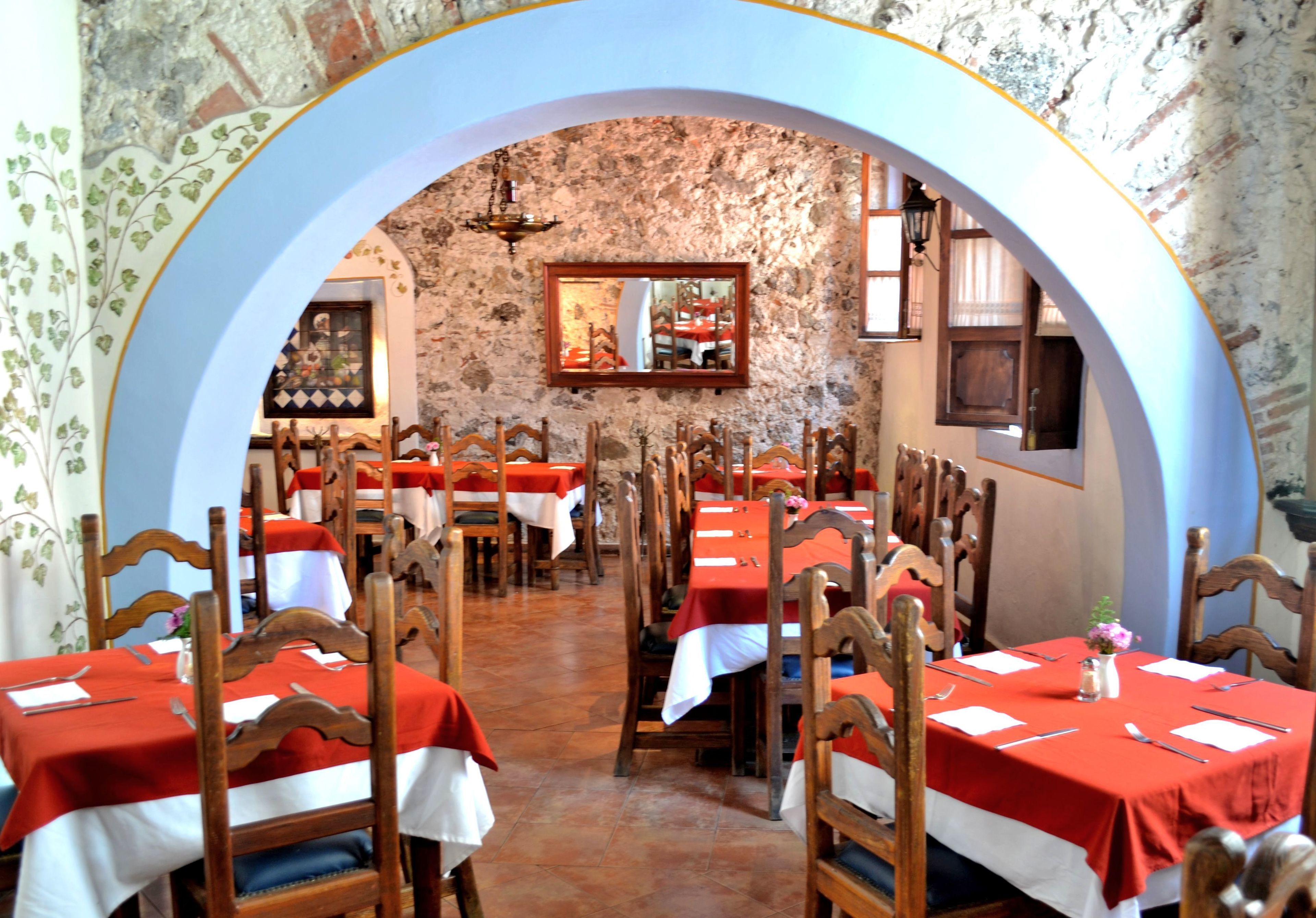 Un ristorante con tavoli apparecchiati, sedie di legno e una parete in pietra.