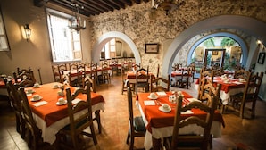 Un restaurant doté de nombreuses tables et chaises, de murs en pierre et d’entrées en arc de cercle.