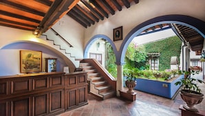 Un hall d’entrée avec un comptoir de réception en bois, un escalier et une vue sur un jardin, accessible par une arche.