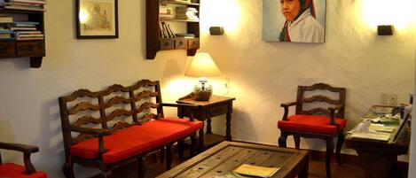 A room with two wooden chairs with red cushions, a wooden coffee table, a bookshelf, and a painting on the wall.