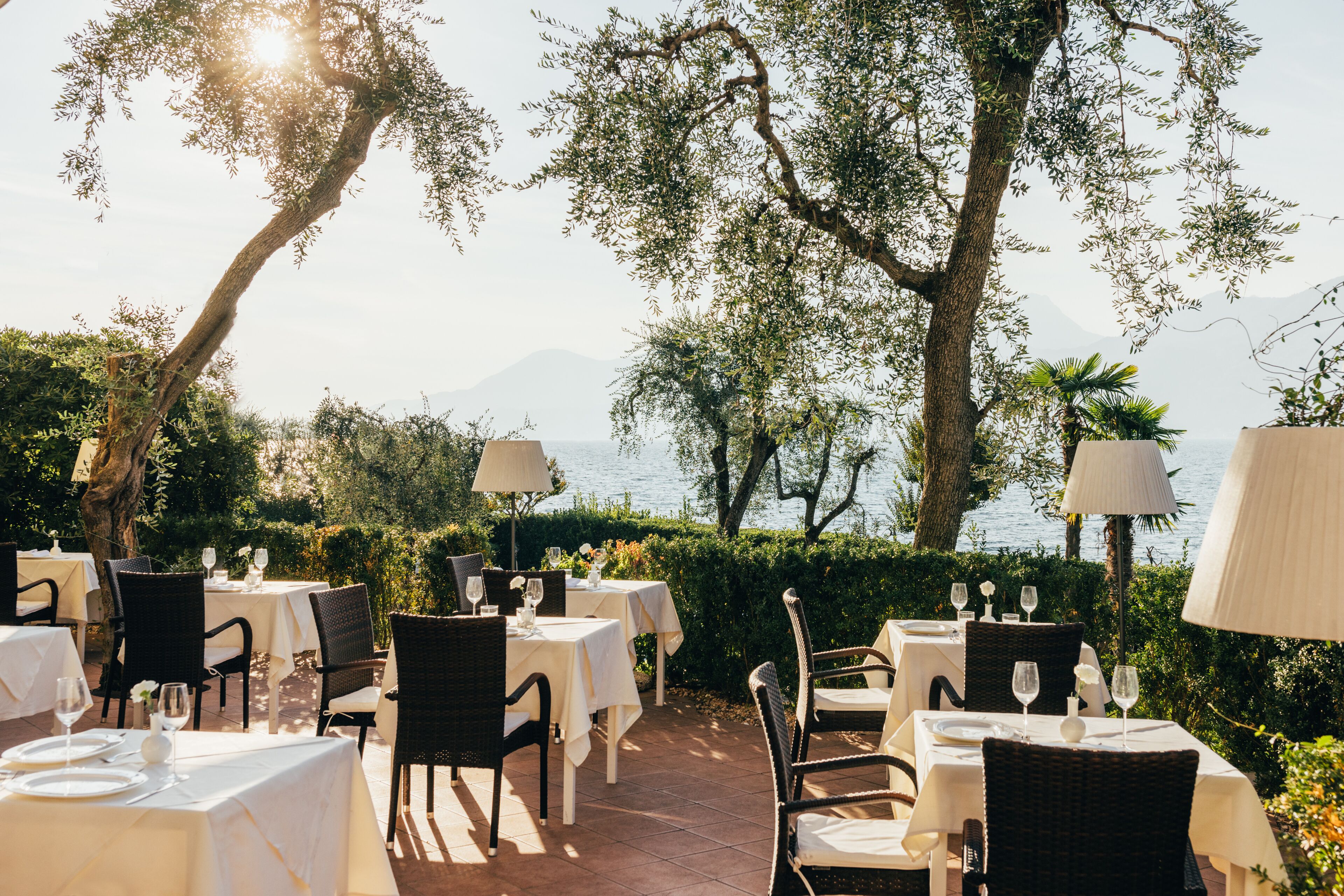 Un espace de restauration en plein air, avec des tables et des chaises, offrant une vue sur un plan d’eau et des montagnes.