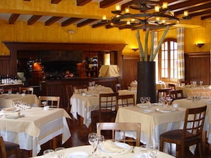 Um restaurante com várias mesas preparadas para refeições, um espaço de bar e um grande vaso decorativo.