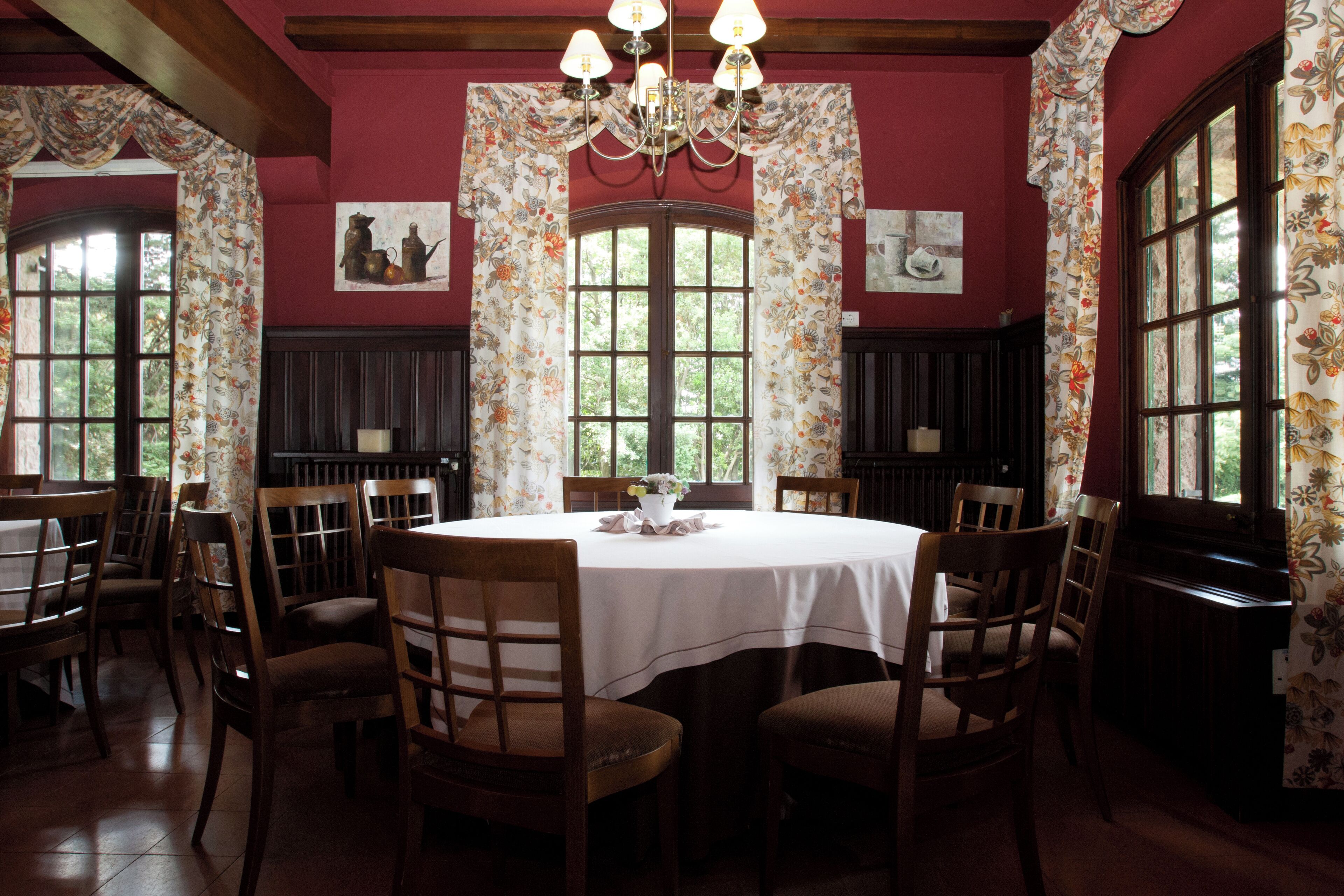 Une salle à manger avec une table ronde, des chaises en bois, des rideaux à motifs floraux et un lustre.