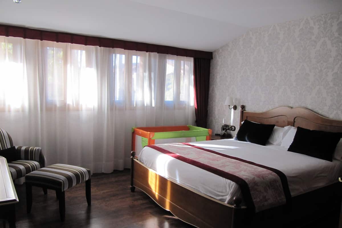 Una habitación de hotel con una cama grande, una mesita de noche de madera, una silla y una pequeña mesa.