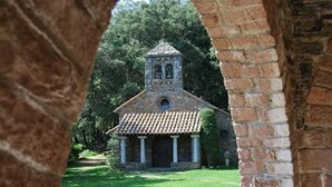 A small stone church with a bell tower, surrounded by greenery and viewed through an archway. - Husa Sant Bernat (Montseny)