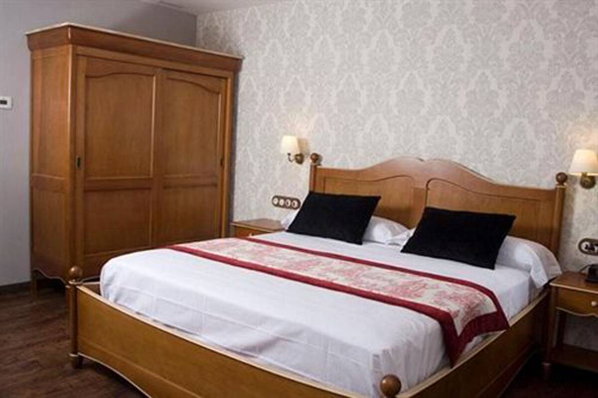 Una cama bien hecha con tablero de madera, dos lámparas de noche y un amplio armario de madera.