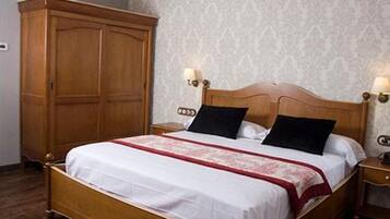 A neatly made bed with a wooden headboard, two bedside lamps, and a large wooden wardrobe.