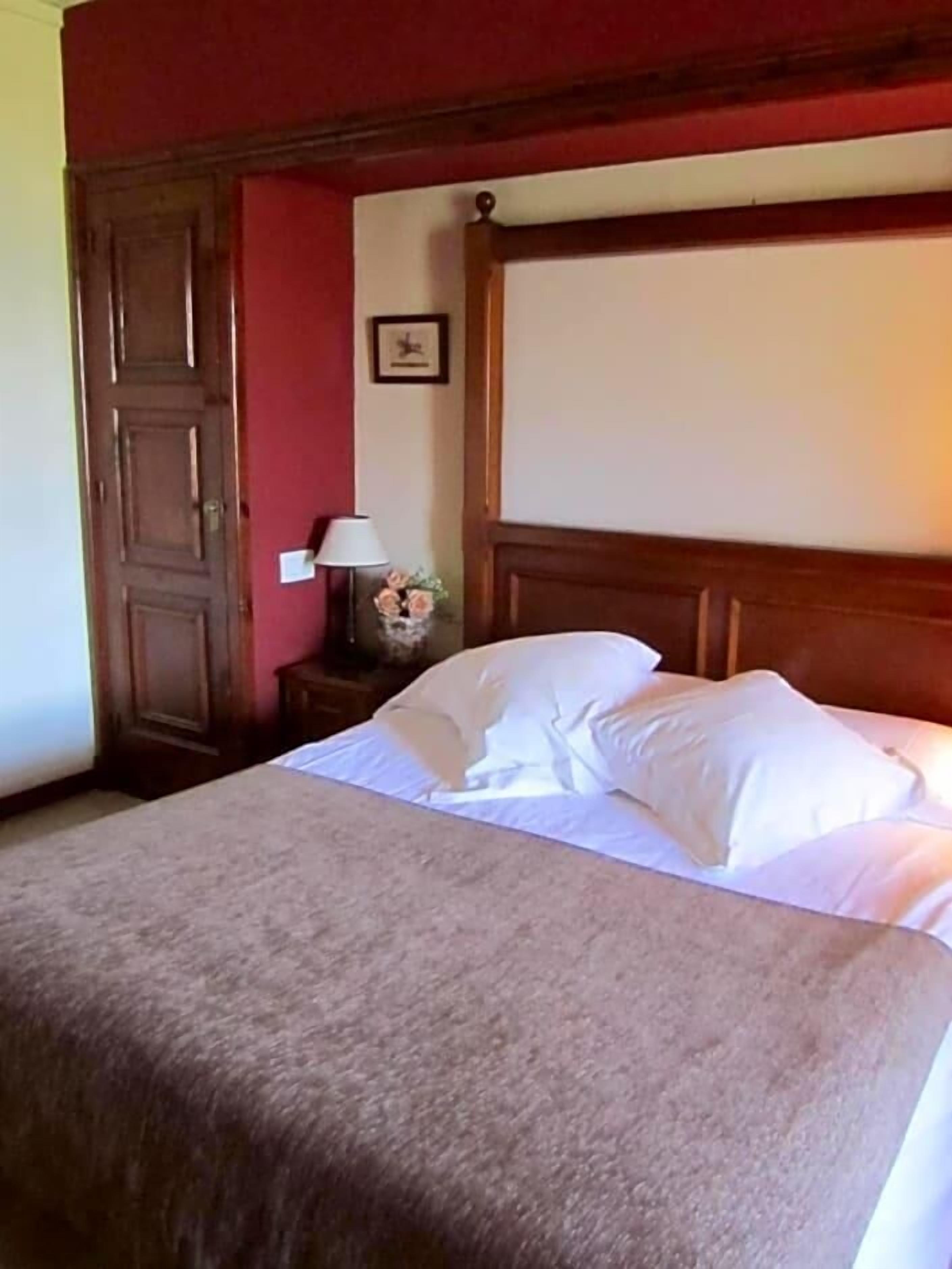 Una habitación de hotel con una cama grande, cabecera de madera, mesita de noche con lámpara y un cuadro enmarcado en la pared.