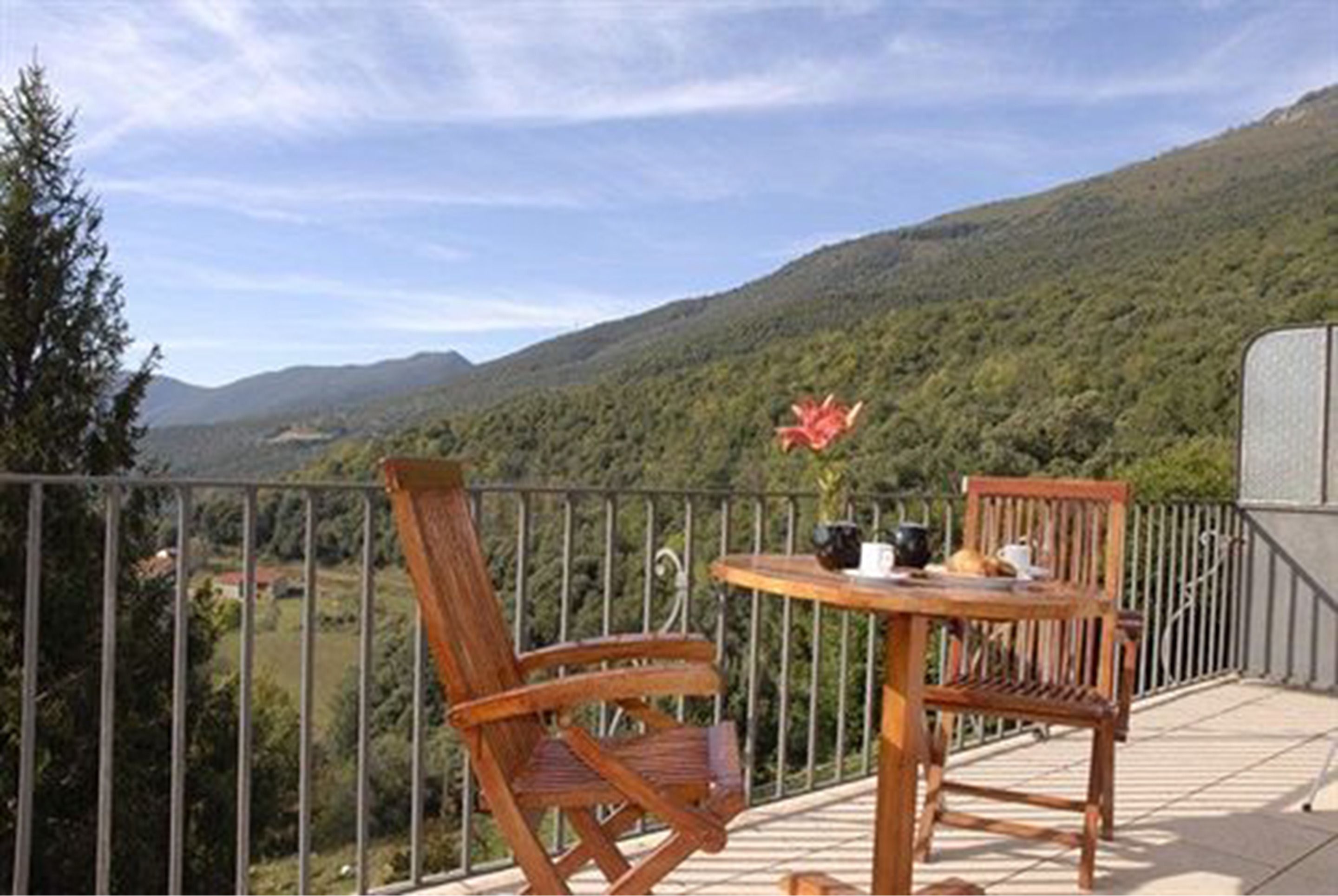 Un balcón con dos sillas de madera y una mesita, con vistas a un paisaje montañoso.