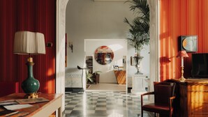 A hotel lobby with a checkered floor, a reception desk, a green lamp, and a large mirror. - Hotel Palazzo Guiscardo (Pietrasanta)