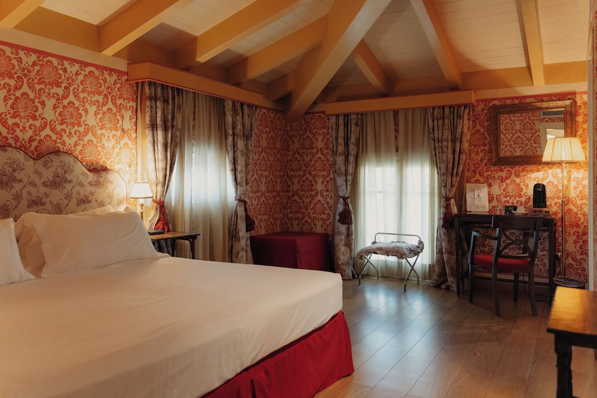 A hotel room with a large bed, a desk, a chair, and a small table.