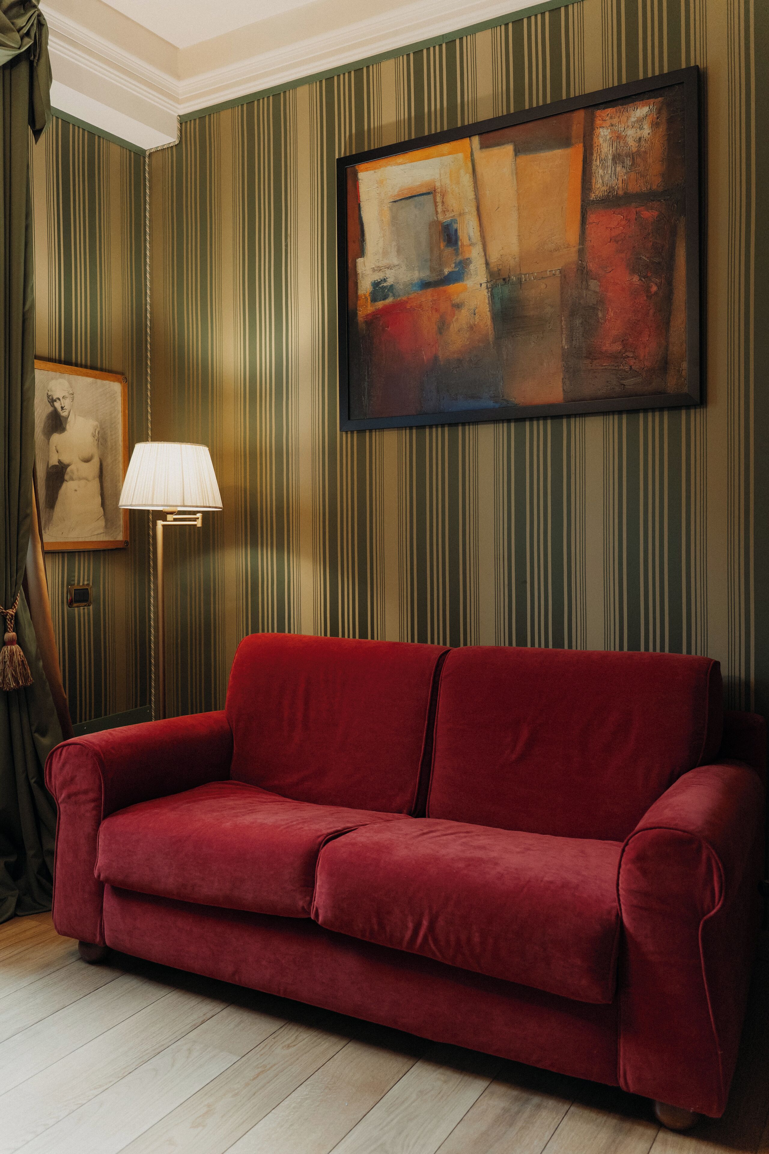 A red sofa in a room with striped wallpaper and a painting on the wall.