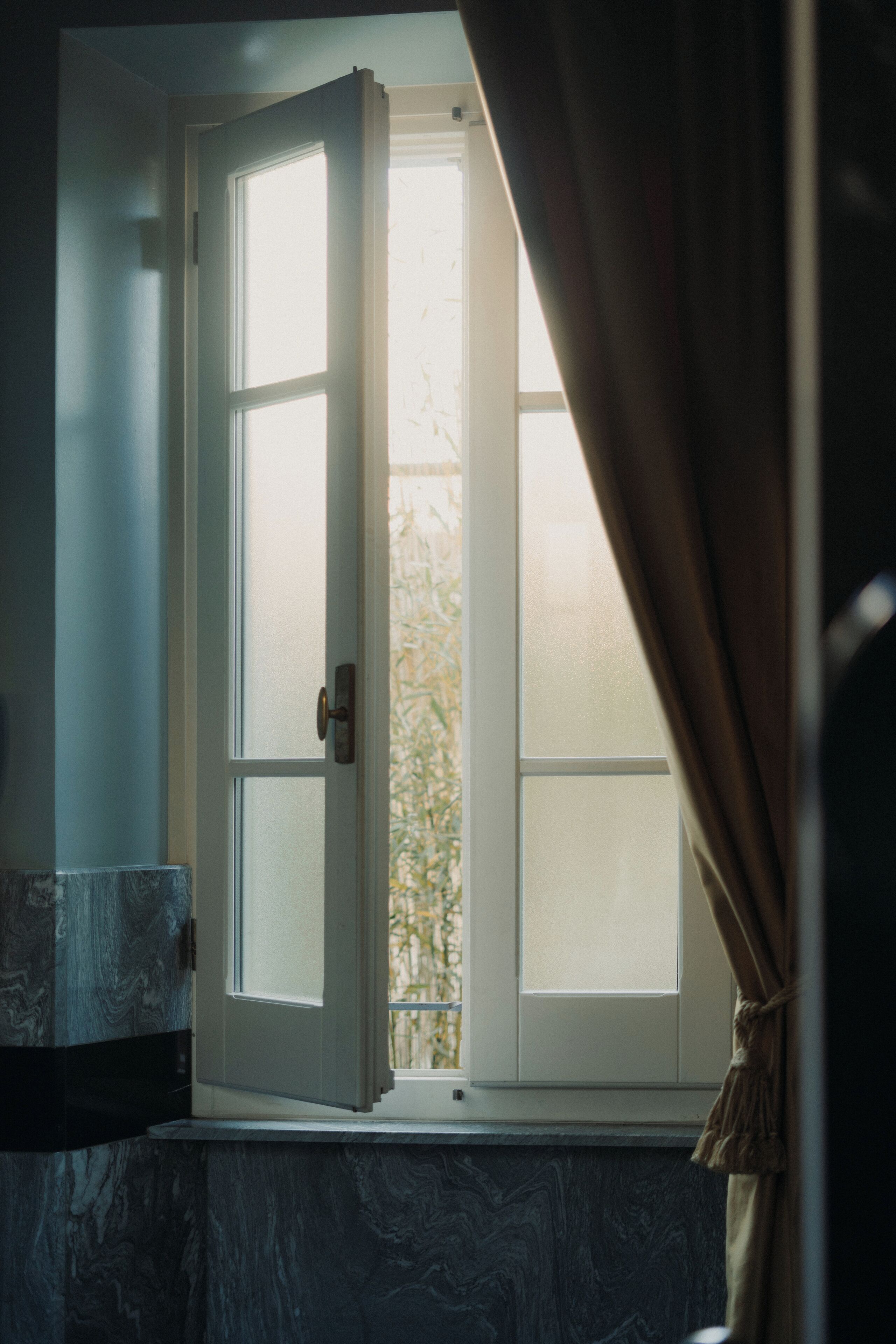 Un baño con puerta blanca, ventana con vidrio esmerilado y encimera de mármol.